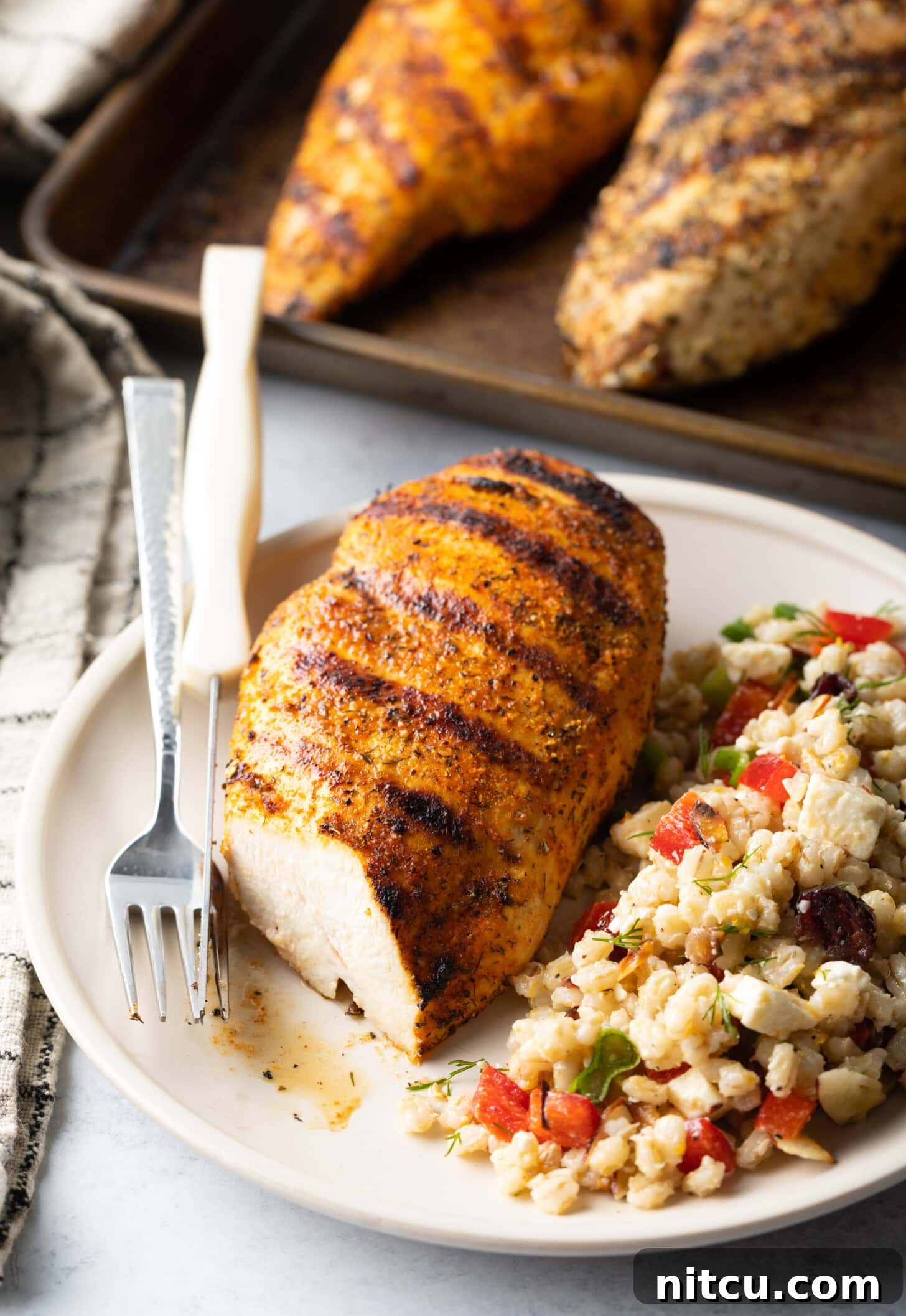 Seasoned grilled chicken breast on a plate. Chicken is cut in half to show inside of the meat. Next to the chicken is a serving of bean salad.