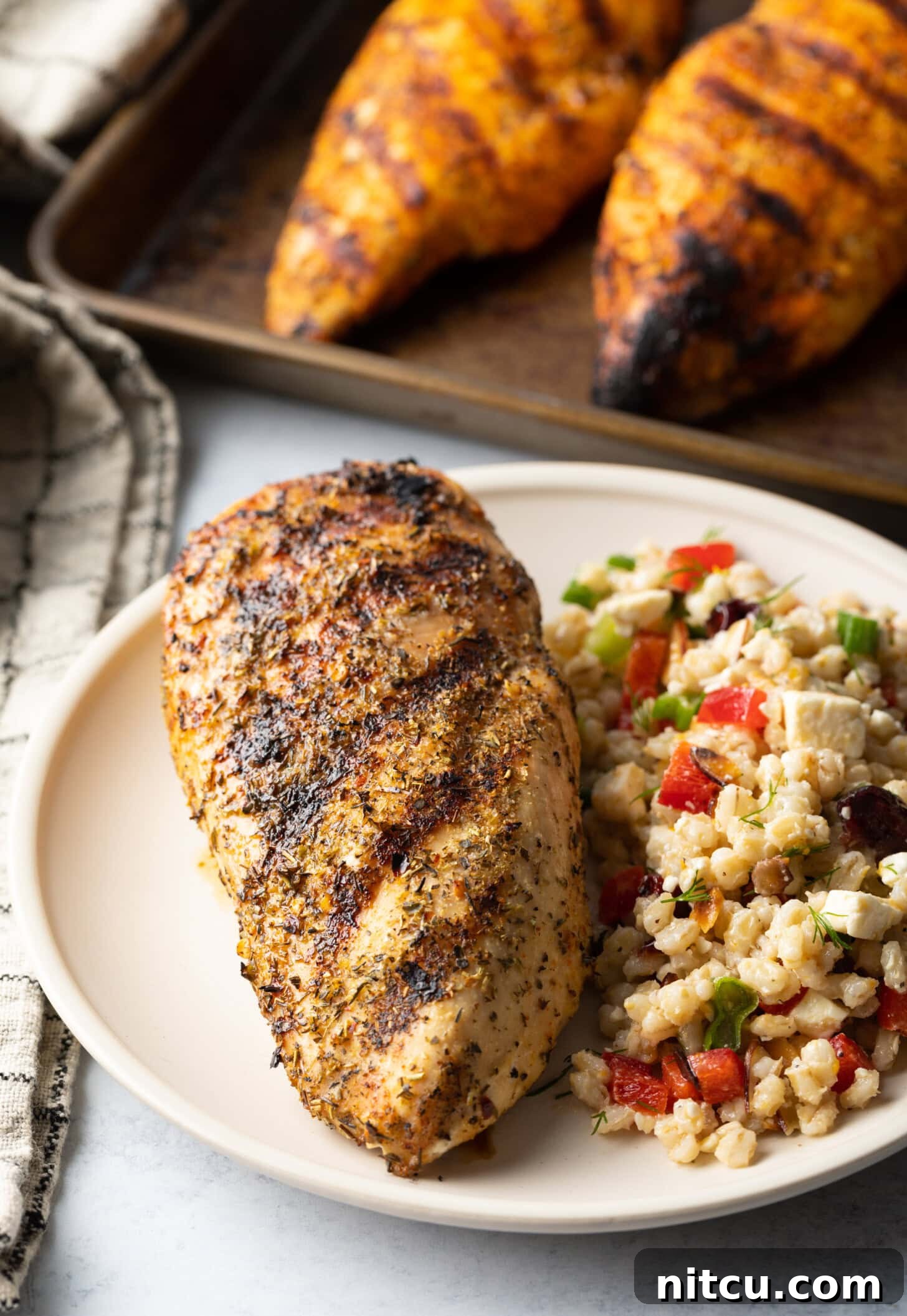 Top down view one whole chicken breast seasoned and grilled, resting on a white plate next two a side of bean salad.