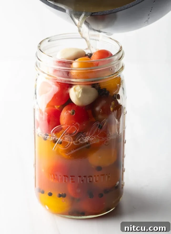Adding pickling liquid to large glass jar filled with small red and yellow tomatoes.