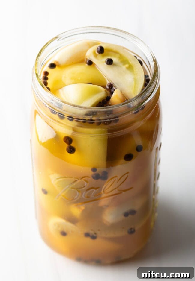 Marinated pickled green peppers in a large glass jar.