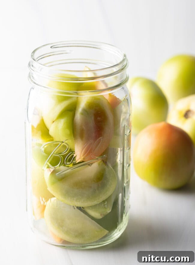 Small green tomatoes in a large glass ball jar.