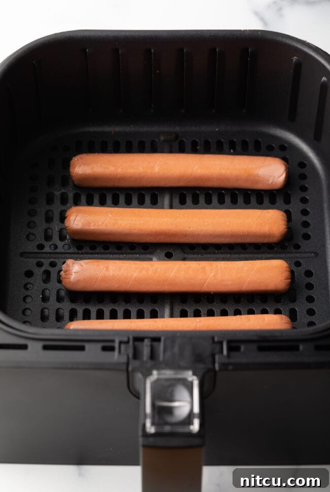 Top down four hot dogs in air fryer basket.