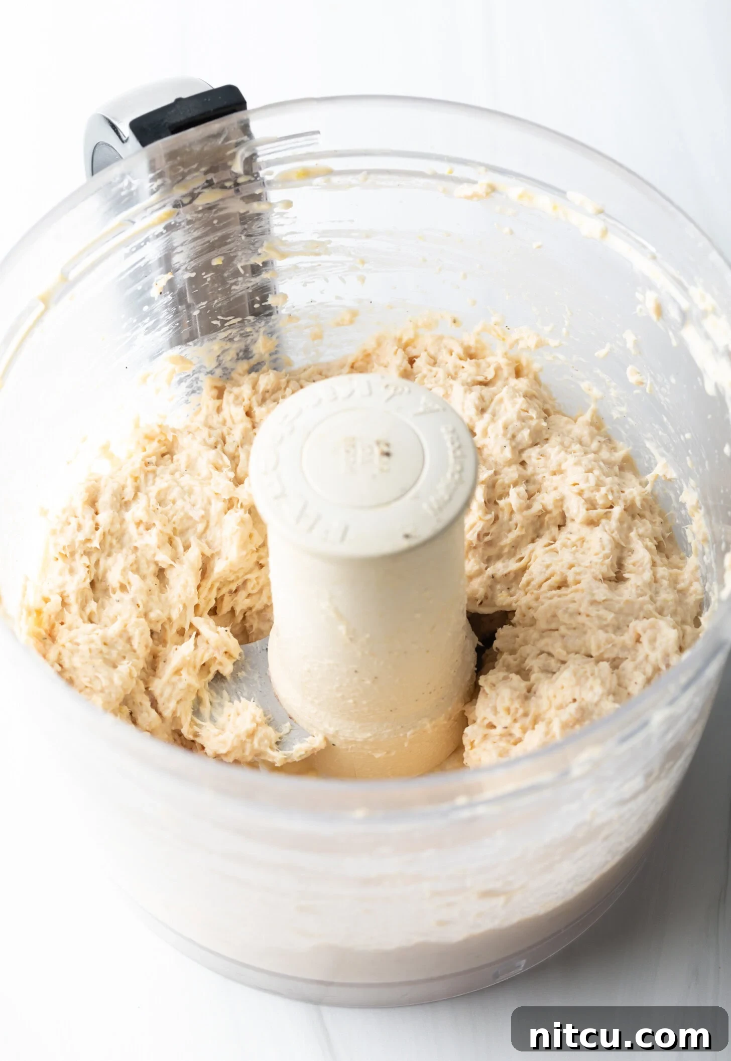 An overhead view captures the creamy, blended smoked fish dip swirling within the clear bowl of a food processor, showcasing its rich texture and readiness.