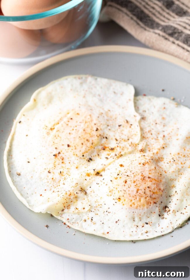 Two cooked eggs over easy on a light blue plate, sprinkled with spices.