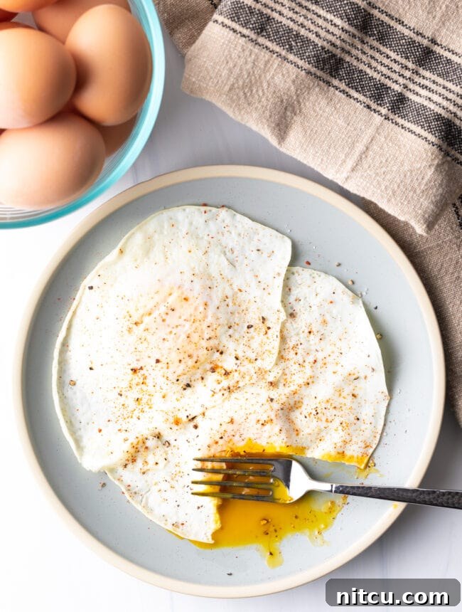 Fork cutting into the soft yolk of a gently over easy fried egg, on a light blue plate.