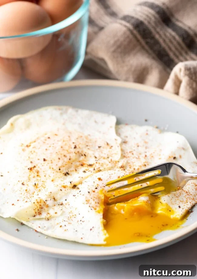 Fork cutting into the soft yolk of a gently over easy fried egg, on a light blue plate.
