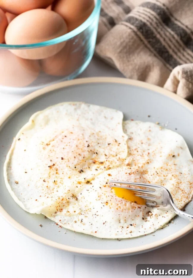 Fork cutting into the soft yolk of a gently over easy fried egg, on a light blue plate.