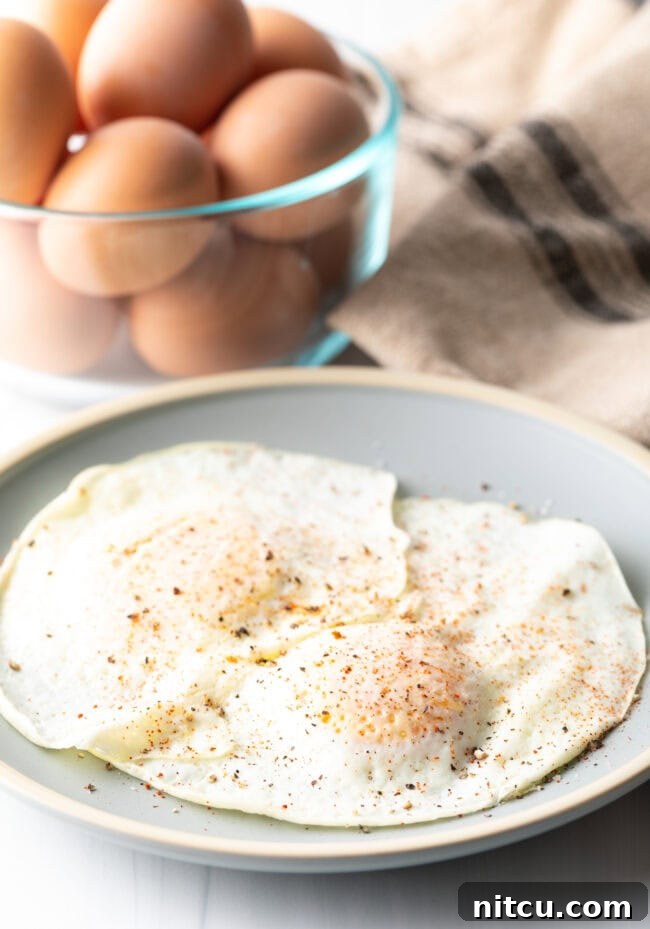 Two cooked eggs over easy on a light blue plate, sprinkled with spices.