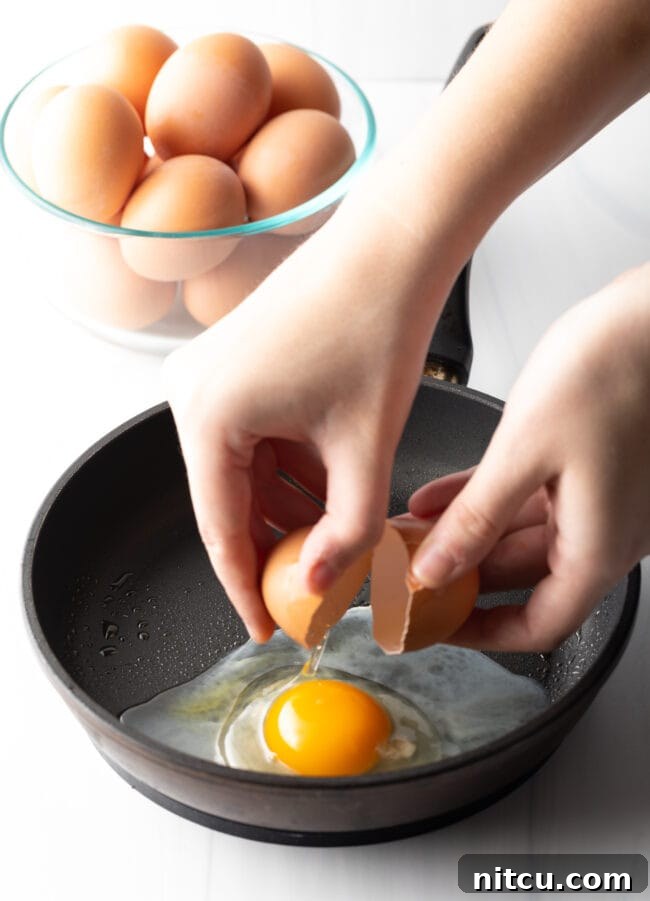 Hands cracking an egg just above a black frying pan.