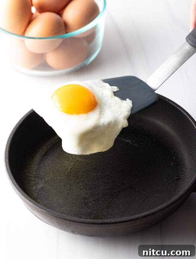 Flipping a fried egg with a black spatula over a black skillet.