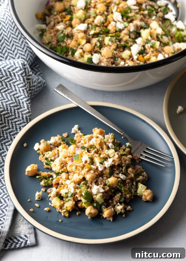 Blue plate with a generous serving of Jennifer Aniston bulgur wheat salad, with a metal fork on the plate.