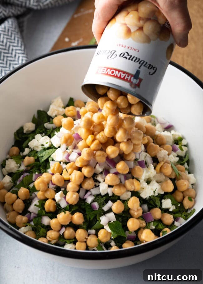Can of chickpeas being dumped into the large white bowl with other ingredients.