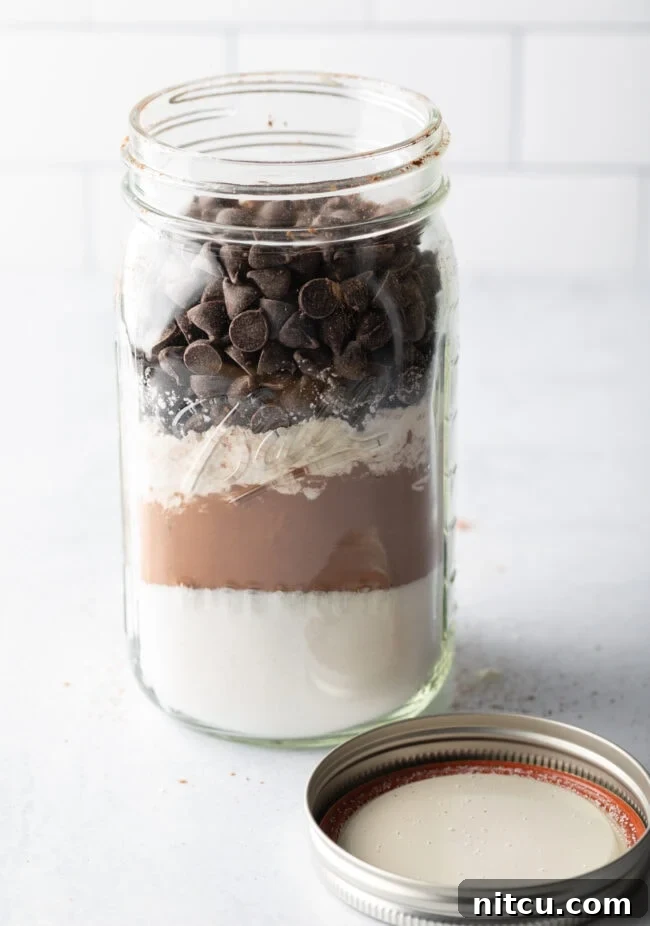 Homemade Ghirardelli brownie mix, dry ingredients layered in a large mason jar with lid off and next to the jar.