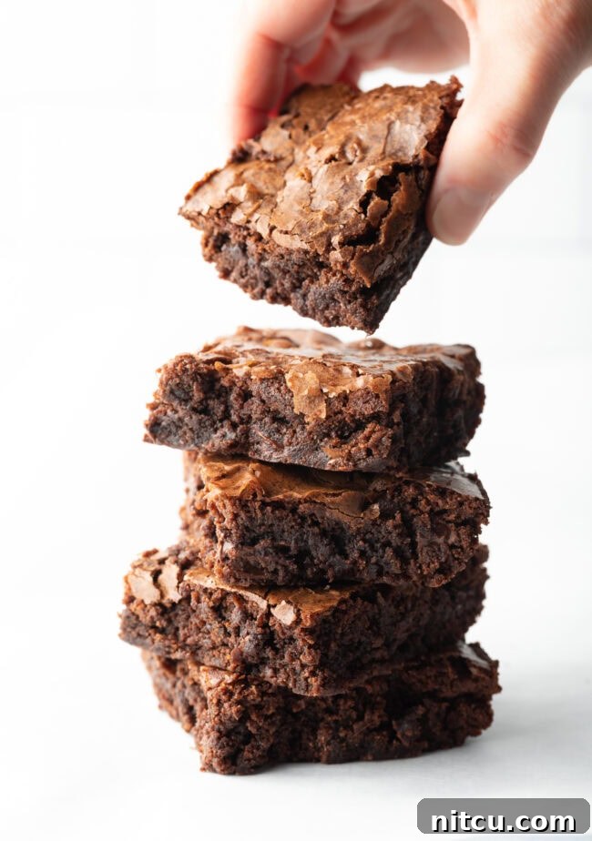 Hand removing a brownie from the top of a stack of 4 remaining brownies.