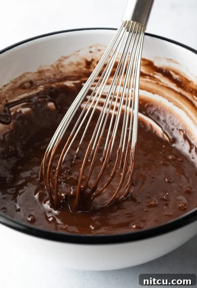 Metal whisk combining wet and dry ingredients into a dark batter.