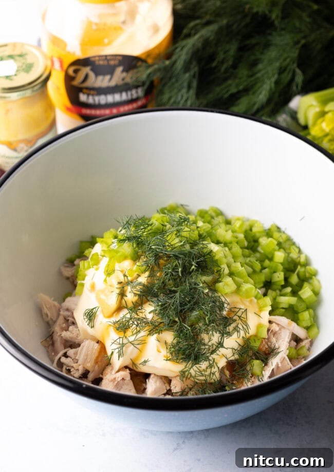 White bowl with shredded poultry, mayo, celery, and fresh dill.