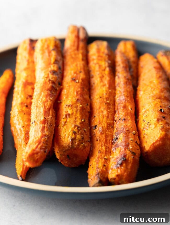 Top down view vertical pile of air fryer roasted carrots on a round black plate.