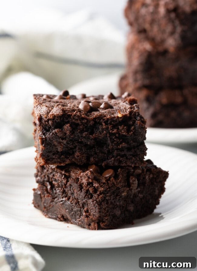 Two collagen protein brownies stacked on a white plate, showcasing their fudgy texture and delicious appearance.