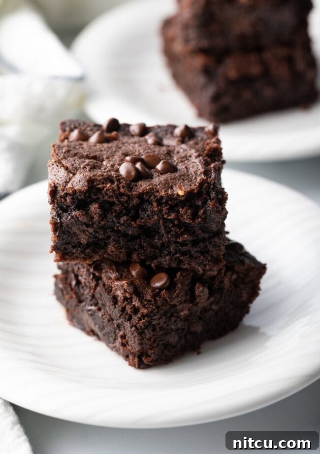 Two brownies with protein collagen stacked on a white plate, highlighting their rich chocolate flavor and tempting texture.