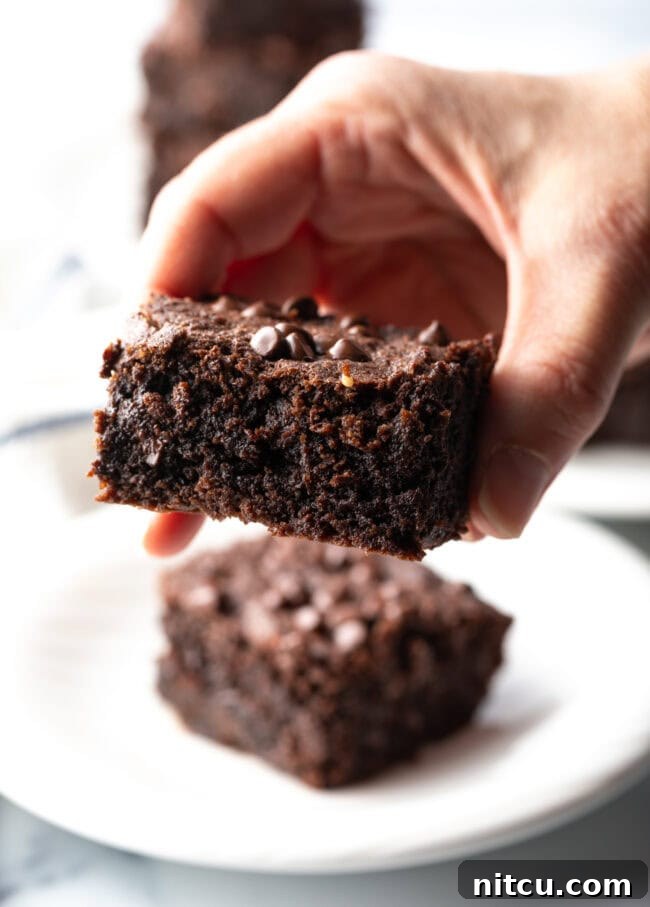 A hand holding a fudgy protein brownie to the camera, showcasing its moist interior and tempting texture.