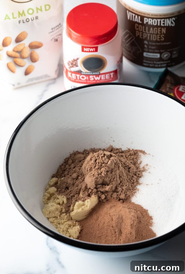 Dry ingredients in a white bowl: cocoa powder, collagen, sweetener alternative, and almond flour, perfectly measured and ready to mix.