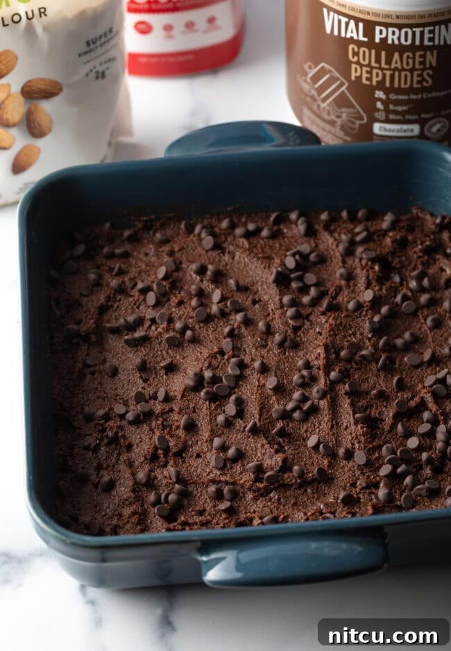 Brownie batter spread into a square baking pan, topped with chocolate chips, ready for the oven.
