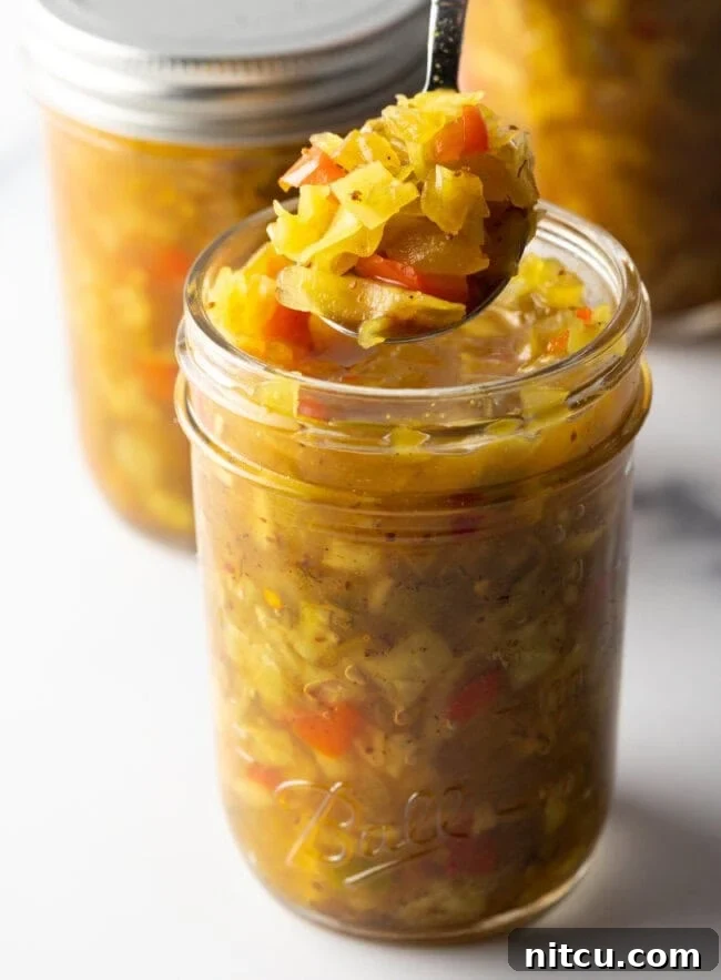 Glass jar of southern chow chow recipe. The lid is off and to the right side, a metal spoon is in the jar showing a scoop to camera.