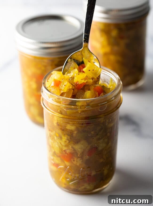 Glass jar of southern chow chow. The lid is off and to the right side, a metal spoon is in the jar showing a scoop to camera.