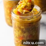 Glass jar of southern chow chow. The lid is off and to the right side, a metal spoon is in the jar showing a scoop to camera.
