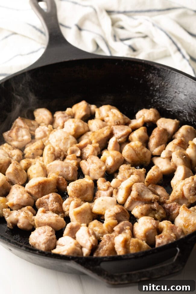Succulent chopped chicken thigh pieces sizzle and stir-fry in a hot cast iron skillet, browning beautifully for the Hunan Chicken.