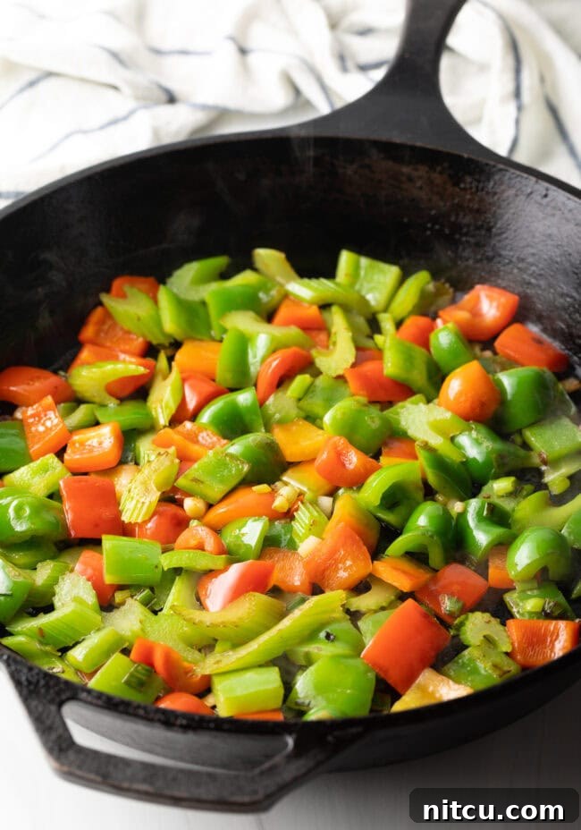 Vibrant chopped red and green bell peppers are stir-frying in a cast iron skillet, adding color and flavor to the dish.