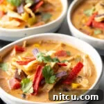 Three white and gray bowls filled with chicken taco soup. Each bowl is garnished with cilantro and red tortilla strips.