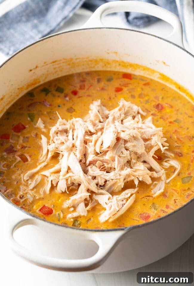 Creamy chicken, bean, and corn soup cooking in a white pot.