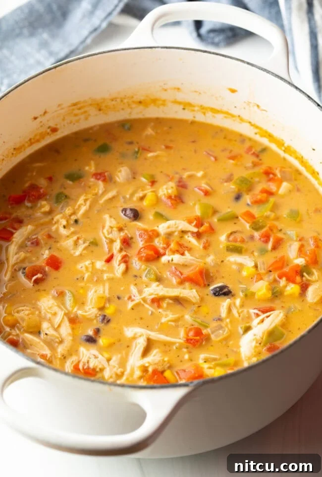 Creamy chicken, bean, and corn soup cooking in a white pot.