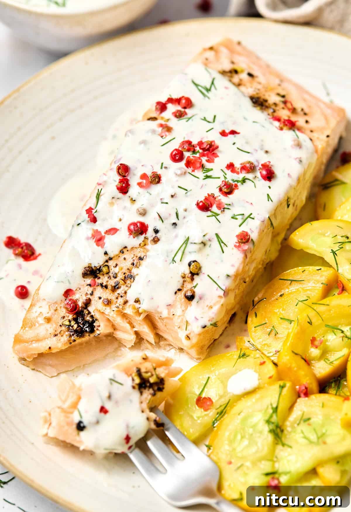Plate with Oven Roasted Salmon with Pink Peppercorn Sauce and yellow squash on the side. A few bites have been taken out of the fish to show the flaky inside. 