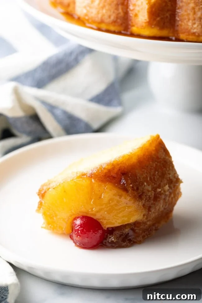 A perfect slice of yellow cake topped with a piece of pineapple and a maraschino cherry, served on a white plate.