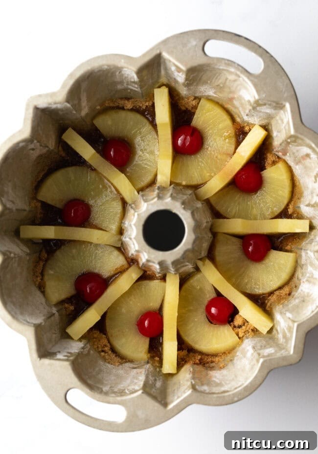 Pineapple slices and bright maraschino cherries carefully arranged in the prepared Bundt pan.