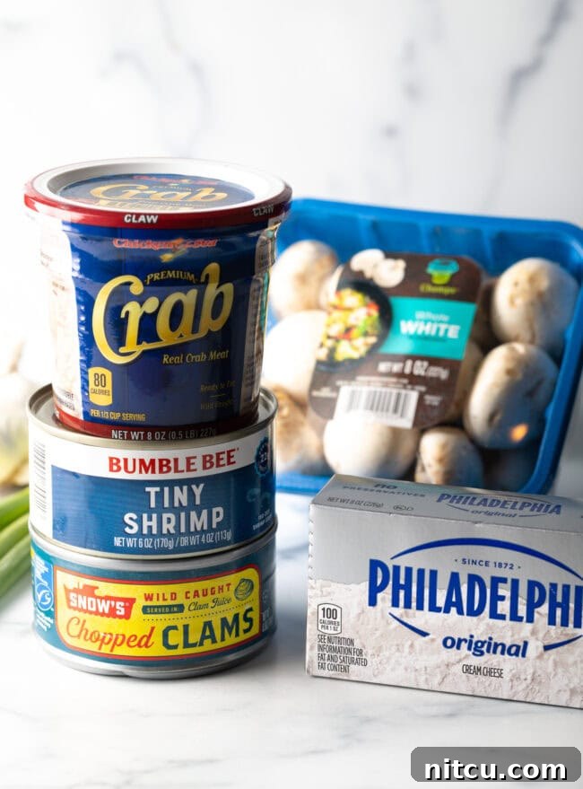 Recipe ingredients: Can of clams, tiny shrimp, and tub of crab stacked on top of each other. A package of cream cheese and package of white mushrooms are next to the stack.