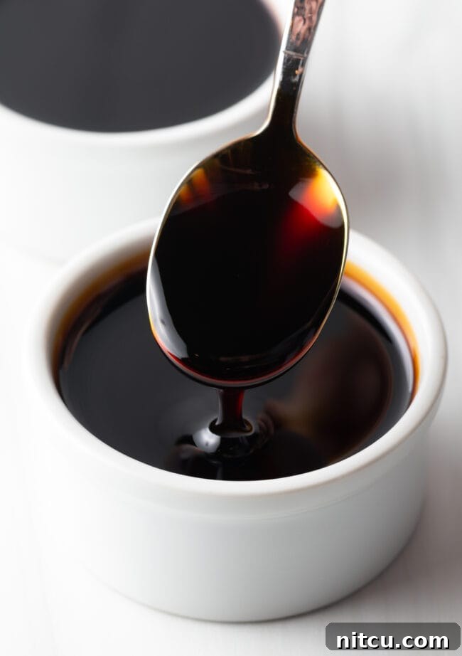 Two white ramekins of eel sauce. One closest to camera has a metal spoon with a spoonful showing to camera.