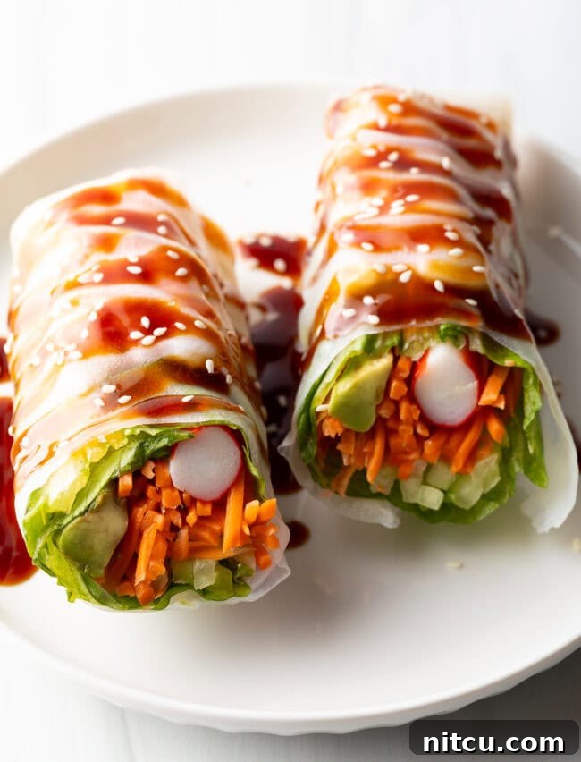 Two veggie spring rolls on a white plate, drizzled with brown sauce.