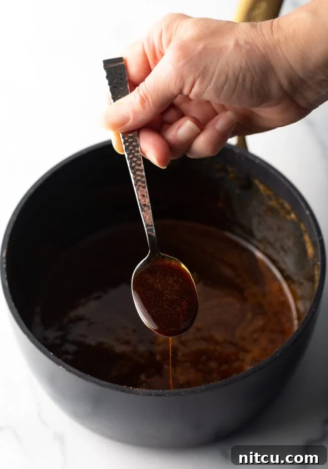 Black sauce pot with eel sauce ingredients. Hand with metal spoon shows spoonful to camera.