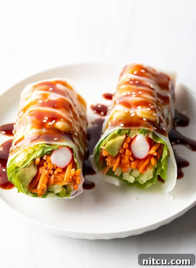 Two veggie spring rolls on a white plate, drizzled with brown sauce.