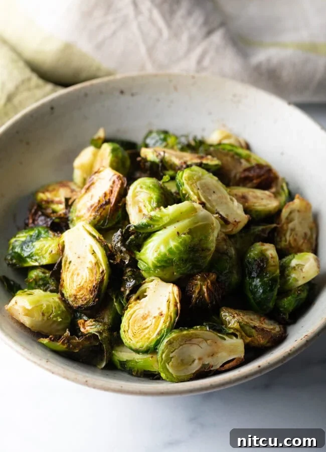 A white bowl brimming with perfectly crispy air fryer Brussels sprouts, showcasing their golden-brown edges and tender appearance.