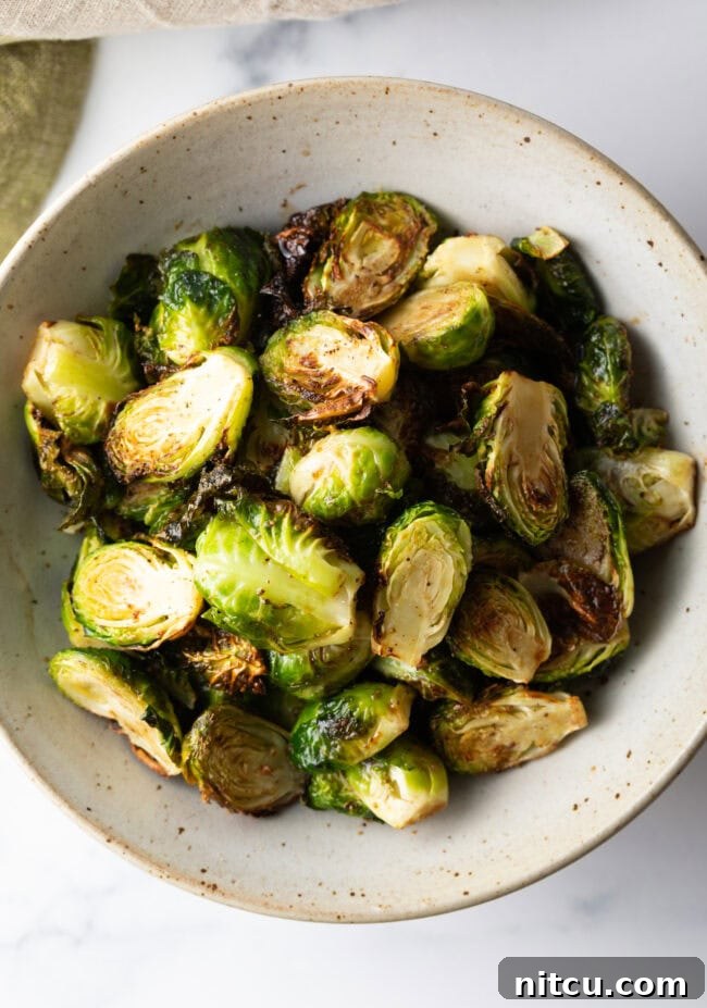 Close-up shot of a white bowl filled with golden-brown, crispy air-fried Brussels sprouts.