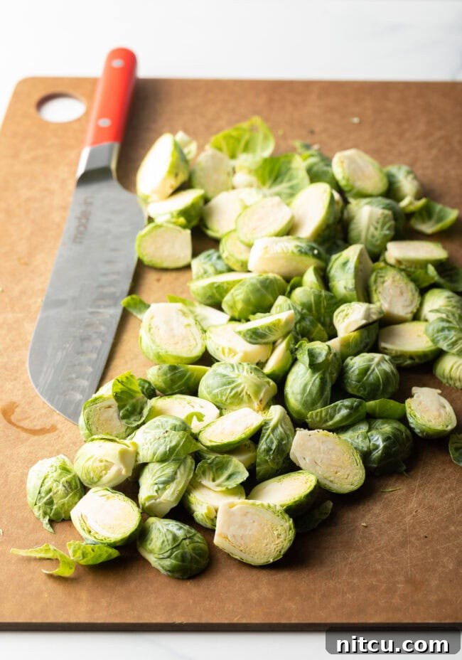Cleaned and halved fresh Brussels sprouts arranged on a brown cutting board, next to a large chef's knife.