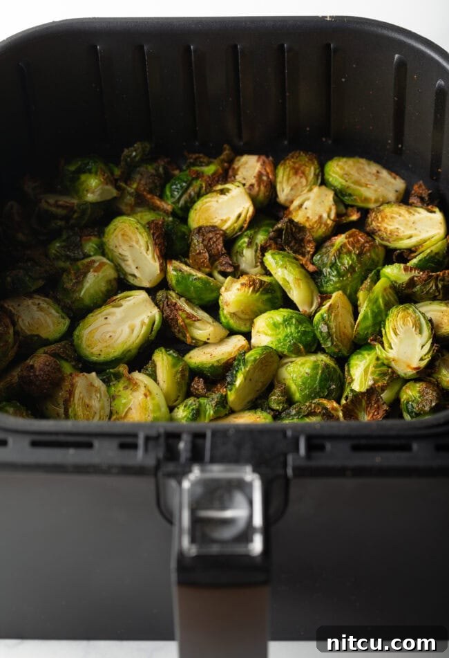 Partially cooked Brussels sprouts halves, starting to crisp, inside an air fryer basket.