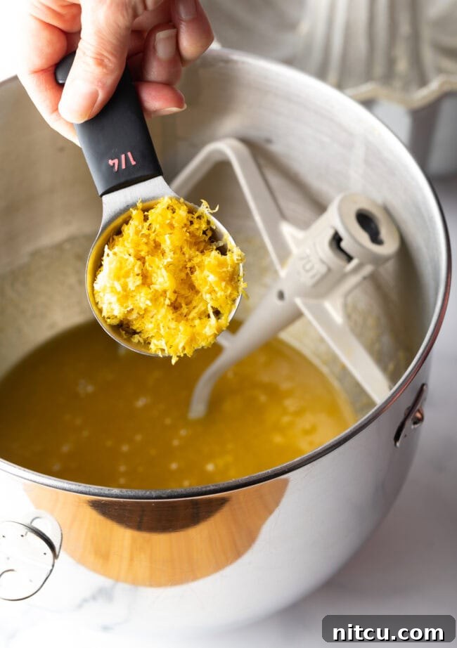 A skilled hand zests a lemon directly into a mixing bowl, capturing every fragrant particle of bright yellow rind, ensuring maximum citrus flavor in the cake batter.