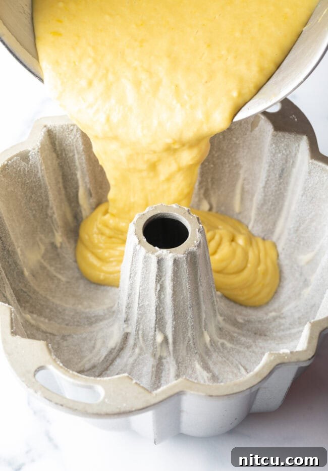 Thick, golden cake batter is carefully poured into a fluted Bundt pan, expertly prepared and ready for baking, promising a beautifully shaped cake.