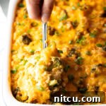Broccoli cheese rice casserole in a white baking dish. A metal spoon is scooping a portion from the dish.