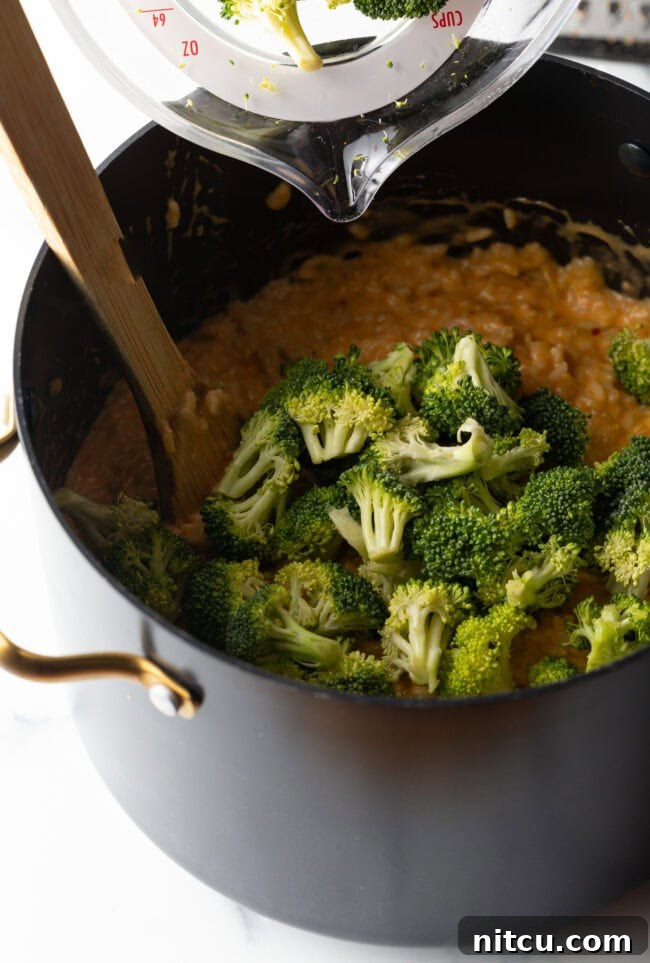 Broccoli florets and cheese in a pot with wooden spoon.